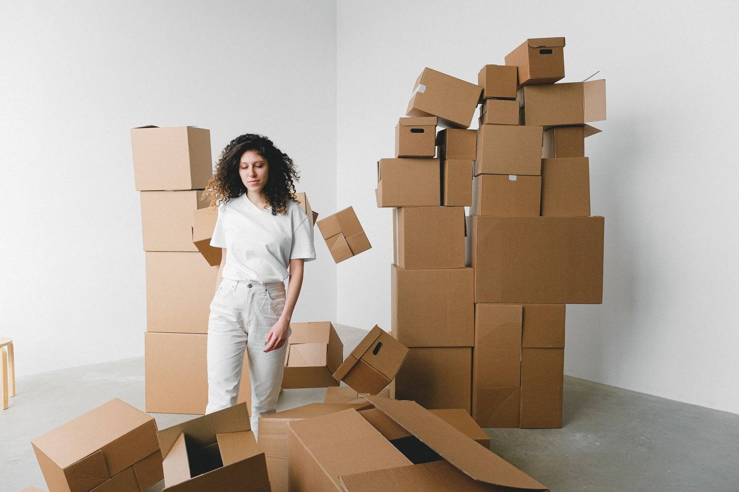 Une jeune femme se tient à l'intérieur, entourée de boîtes en carton empilées.